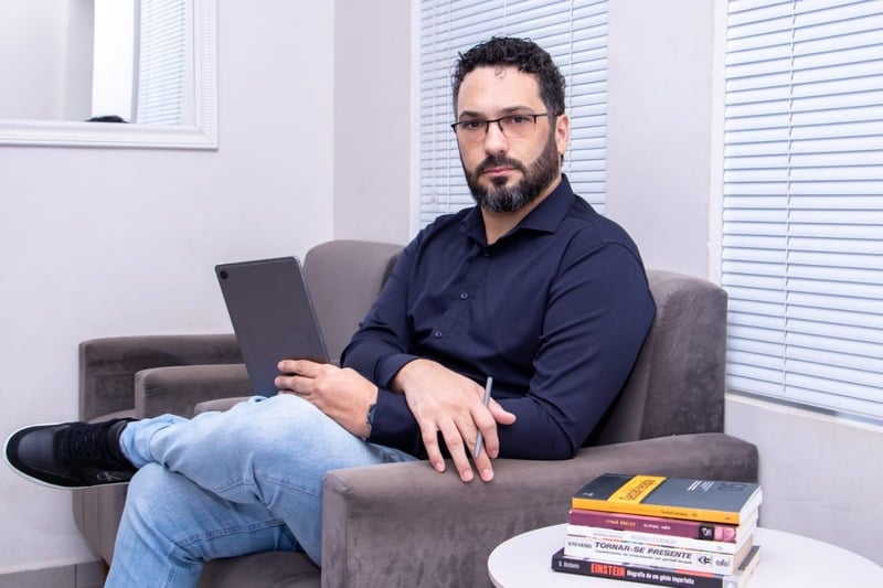 Ricardo Avelar sentado em uma poltrona, segurando um tablet